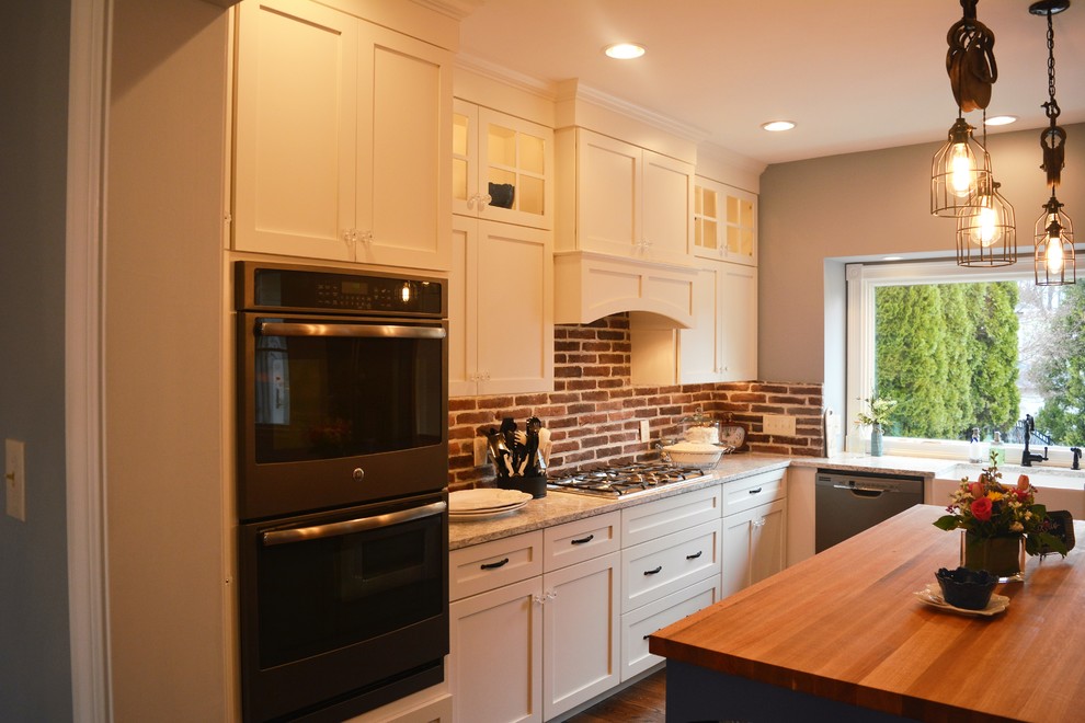 Example of a large cottage l-shaped medium tone wood floor and brown floor eat-in kitchen design in Philadelphia with a farmhouse sink, shaker cabinets, white cabinets, quartz countertops, multicolored backsplash, brick backsplash, stainless steel appliances, an island and multicolored countertops