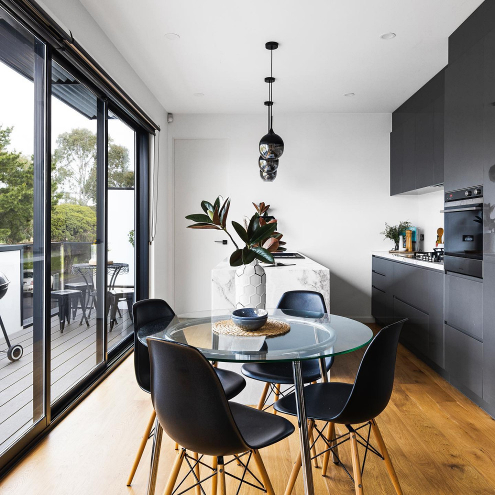 Zweizeilige Moderne Küche mit flächenbündigen Schrankfronten, grauen Schränken, schwarzen Elektrogeräten, braunem Holzboden, Halbinsel, braunem Boden und weißer Arbeitsplatte in Melbourne
