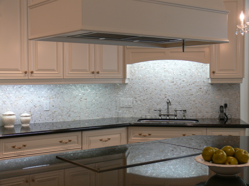 Inredning av ett klassiskt mycket stort kök, med en undermonterad diskho, luckor med upphöjd panel, vita skåp, granitbänkskiva, flerfärgad stänkskydd, rostfria vitvaror, marmorgolv och en köksö