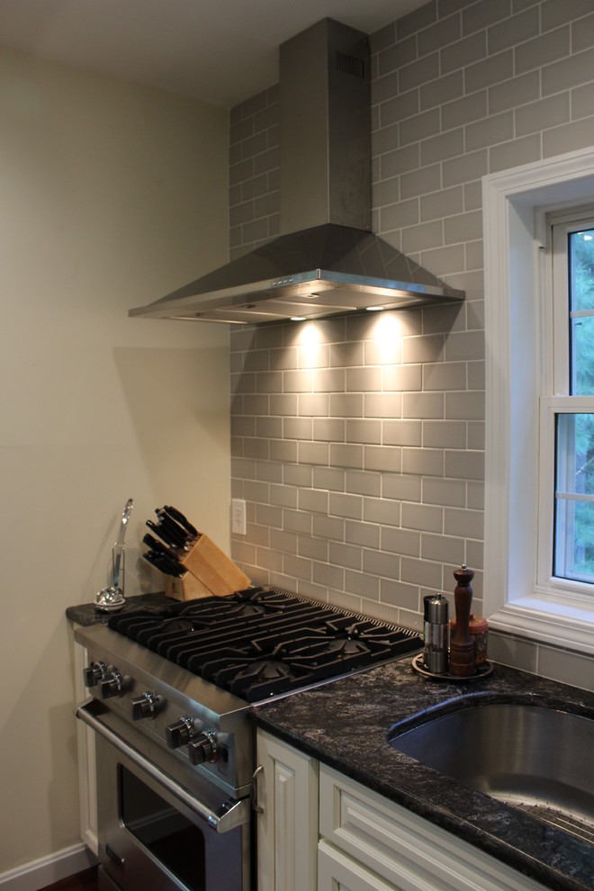 Inredning av ett klassiskt mellanstort kök, med en enkel diskho, luckor med upphöjd panel, vita skåp, granitbänkskiva, grått stänkskydd, stänkskydd i tunnelbanekakel, rostfria vitvaror, mörkt trägolv och flera köksöar