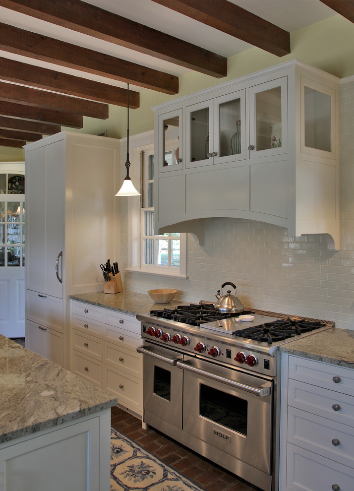 Photo of a farmhouse kitchen/diner in DC Metro with an integrated sink, recessed-panel cabinets, white cabinets, white splashback, metro tiled splashback, stainless steel appliances, brick flooring, an island and marble worktops.