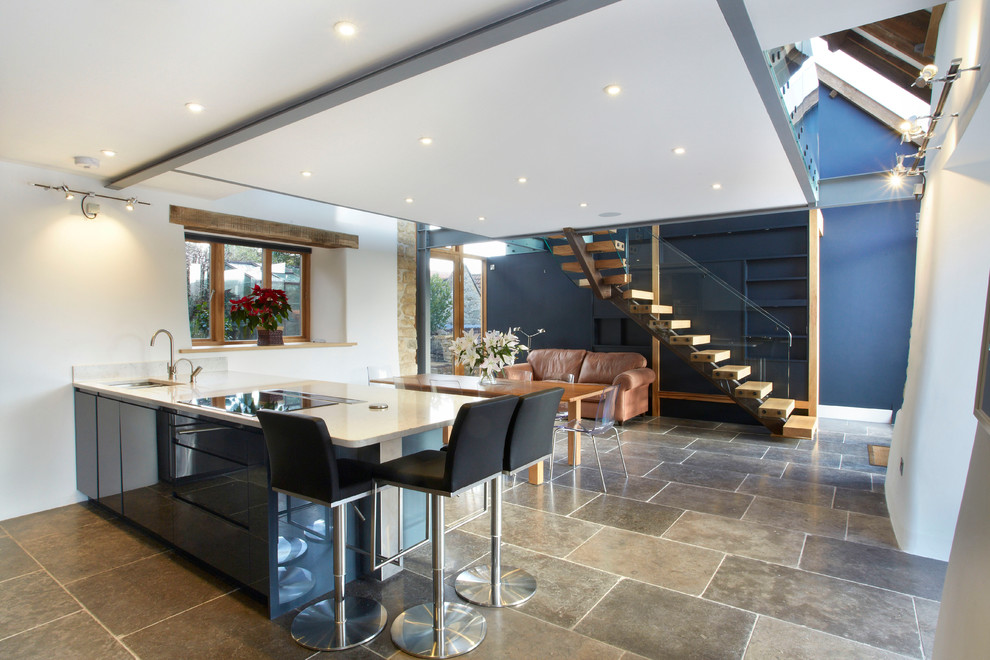 Photo of a large contemporary open plan kitchen in Wiltshire with blue cabinets, a breakfast bar, a double-bowl sink, flat-panel cabinets, composite countertops, white splashback, integrated appliances and porcelain flooring.