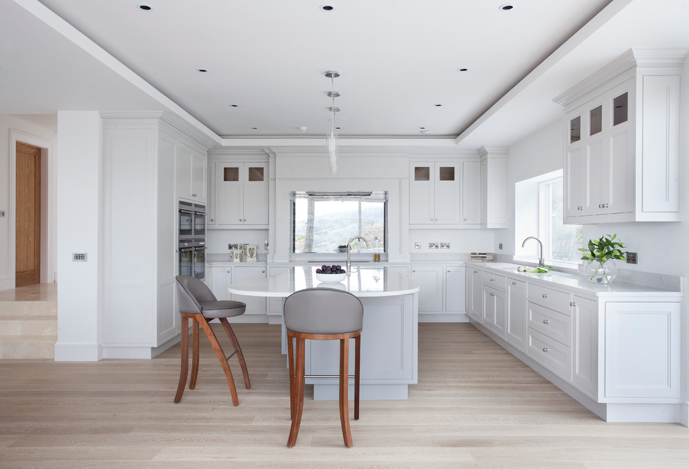 Inspiration for a contemporary u-shaped kitchen/diner in Dublin with a double-bowl sink, beaded cabinets, engineered stone countertops, mirror splashback, stainless steel appliances, medium hardwood flooring and an island.