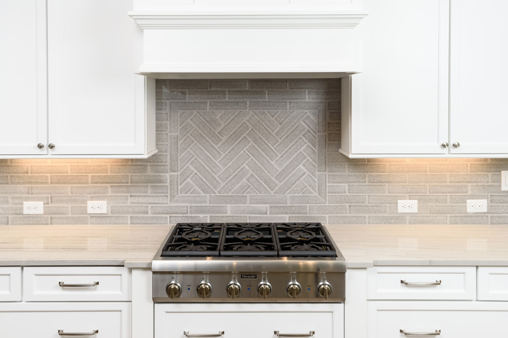 Inspiration for a mid-sized coastal l-shaped light wood floor kitchen remodel in Jacksonville with an undermount sink, shaker cabinets, white cabinets, solid surface countertops, gray backsplash, stone tile backsplash, stainless steel appliances and an island