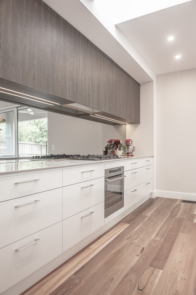 メルボルンにあるコンテンポラリースタイルのおしゃれなキッチン (フラットパネル扉のキャビネット、白いキャビネット、ミラータイルのキッチンパネル、無垢フローリング) の写真