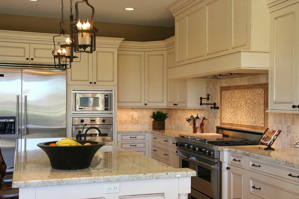 Example of a tuscan l-shaped kitchen design in Dallas with a farmhouse sink, beaded inset cabinets, beige cabinets, granite countertops, beige backsplash, stone tile backsplash, stainless steel appliances, an island and beige countertops