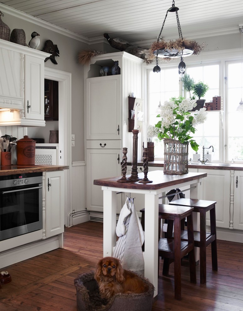 Inspiration for a mid-sized eclectic single-wall dark wood floor eat-in kitchen remodel in Stockholm with raised-panel cabinets, white cabinets, stainless steel appliances, an island and wood countertops