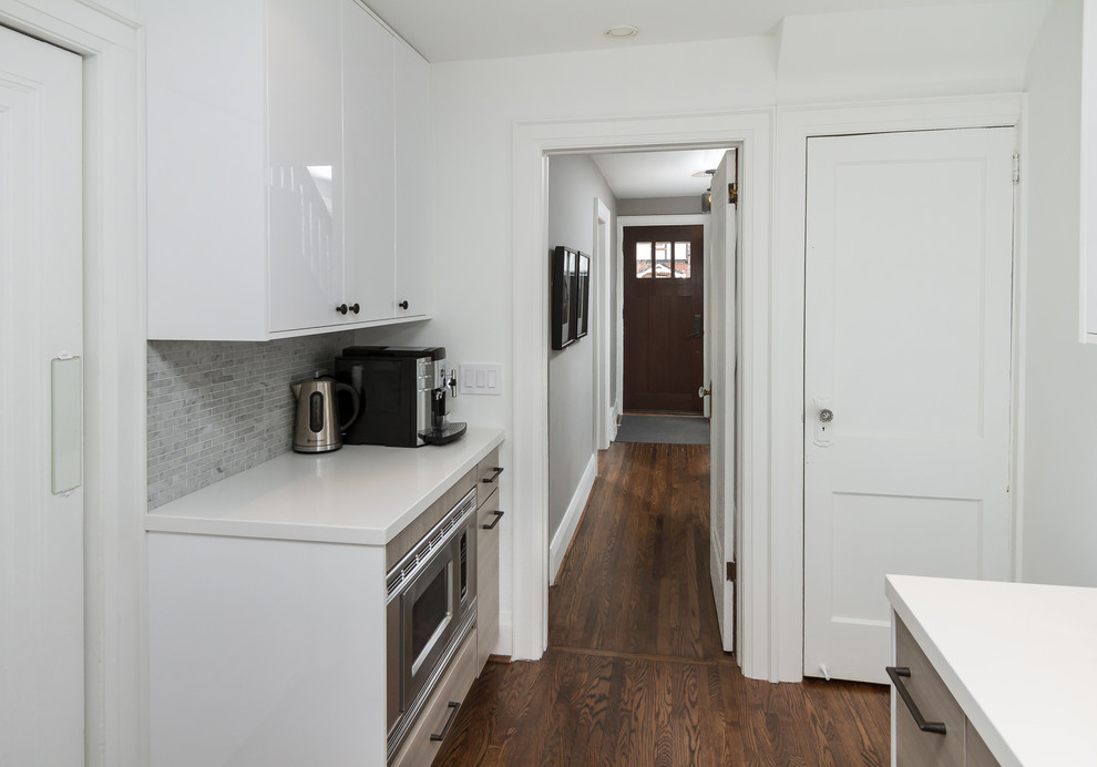 Ejemplo de cocina comedor contemporánea pequeña sin isla con fregadero bajoencimera, armarios con paneles lisos, puertas de armario blancas, encimera de acrílico, salpicadero blanco, salpicadero de azulejos de piedra, electrodomésticos de acero inoxidable y suelo de madera en tonos medios