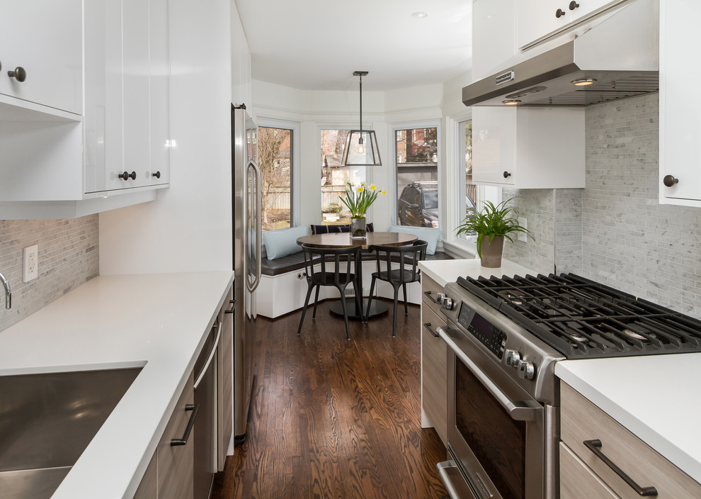 Small trendy galley medium tone wood floor and brown floor eat-in kitchen photo in Toronto with an undermount sink, glass-front cabinets, white cabinets, solid surface countertops, white backsplash, stone tile backsplash, stainless steel appliances and no island