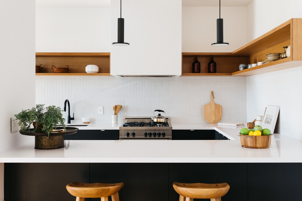 Foto de cocina actual de tamaño medio con fregadero bajoencimera, armarios con paneles lisos, puertas de armario negras, encimera de cuarcita, salpicadero blanco, salpicadero con mosaicos de azulejos, electrodomésticos de acero inoxidable, suelo de madera clara y península