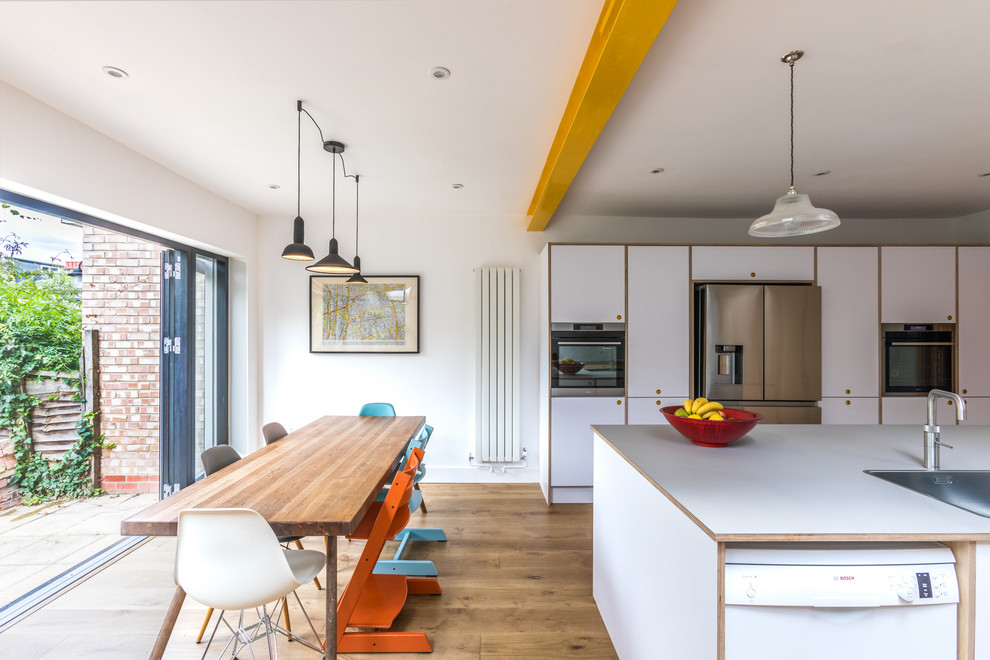 Foto på ett mellanstort funkis vit linjärt kök och matrum, med en integrerad diskho, släta luckor, laminatbänkskiva, grått stänkskydd, stänkskydd i keramik, rostfria vitvaror, korkgolv, en köksö och vita skåp