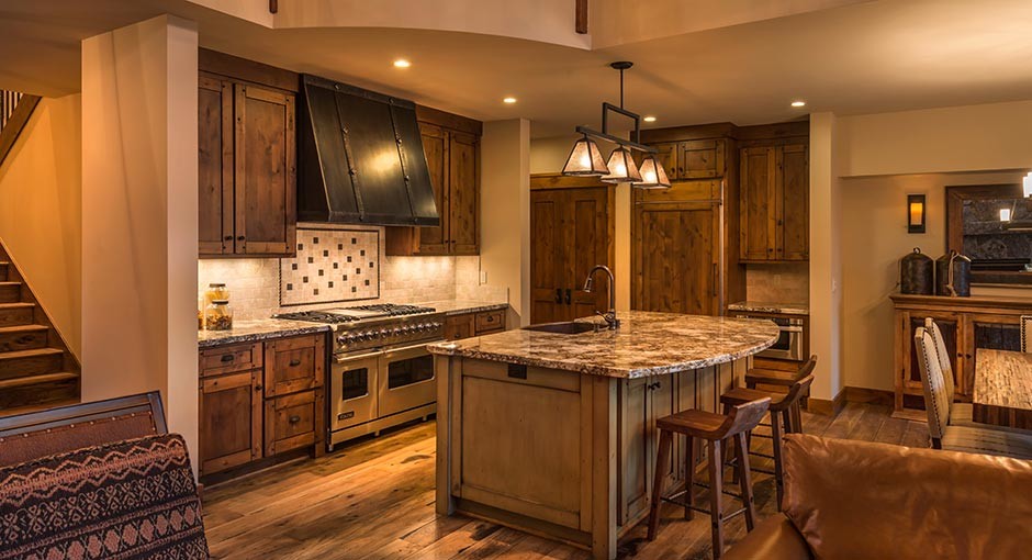 Example of a mid-sized mountain style single-wall dark wood floor eat-in kitchen design in Seattle with an undermount sink, recessed-panel cabinets, dark wood cabinets, granite countertops, beige backsplash, stone tile backsplash, paneled appliances and an island