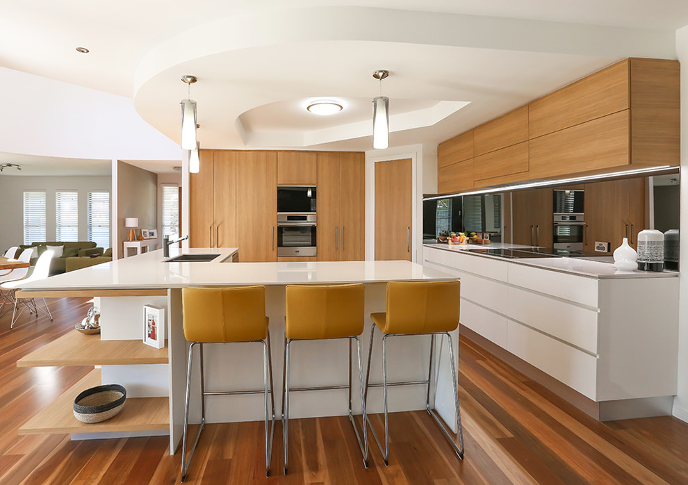 Open concept kitchen - large modern l-shaped brown floor and medium tone wood floor open concept kitchen idea in Brisbane with flat-panel cabinets, light wood cabinets, mirror backsplash, stainless steel appliances, an island, an undermount sink and quartz countertops