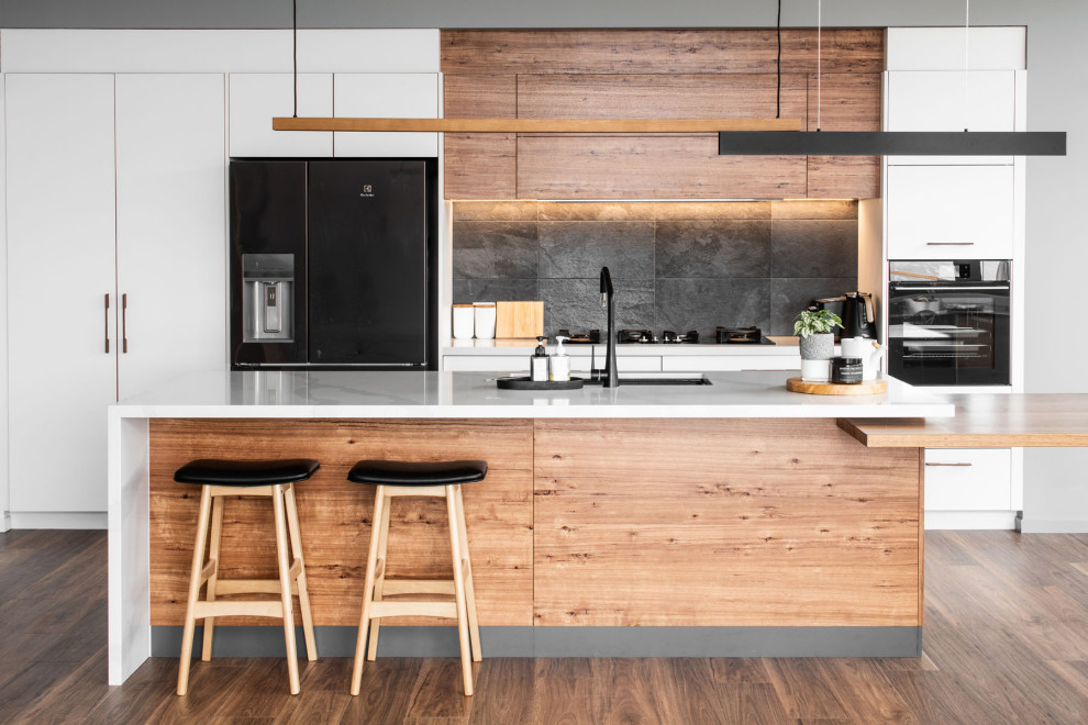 Zweizeilige Moderne Küche mit Unterbauwaschbecken, flächenbündigen Schrankfronten, weißen Schränken, Küchenrückwand in Schwarz, schwarzen Elektrogeräten, dunklem Holzboden, Kücheninsel, braunem Boden und weißer Arbeitsplatte in Hobart