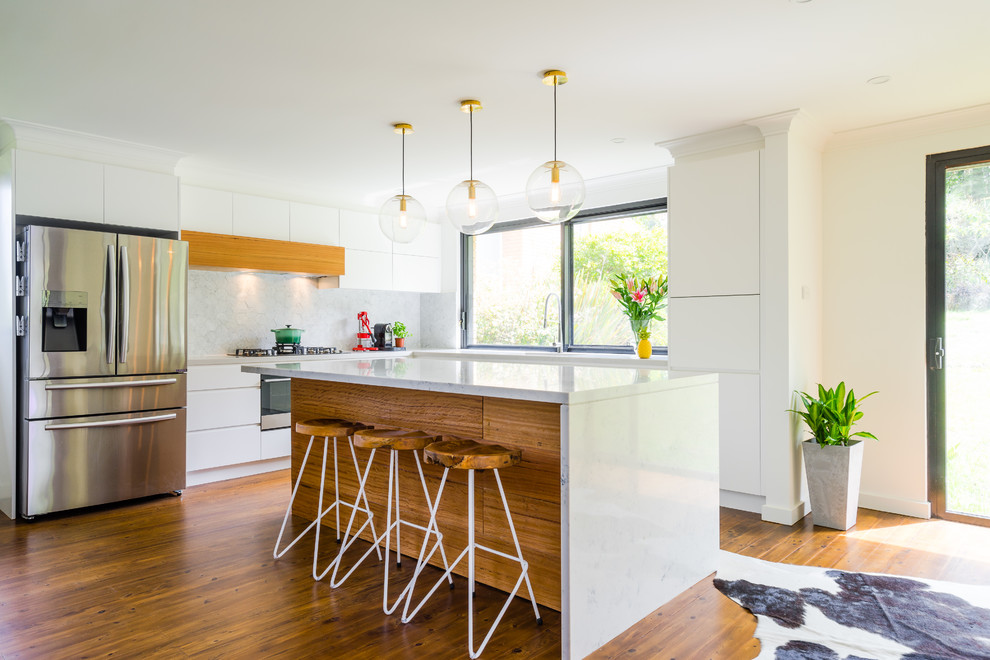 Offene Moderne Küche mit flächenbündigen Schrankfronten, weißen Schränken, Küchenrückwand in Weiß, Küchengeräten aus Edelstahl, braunem Holzboden, Kücheninsel und weißer Arbeitsplatte in Sydney