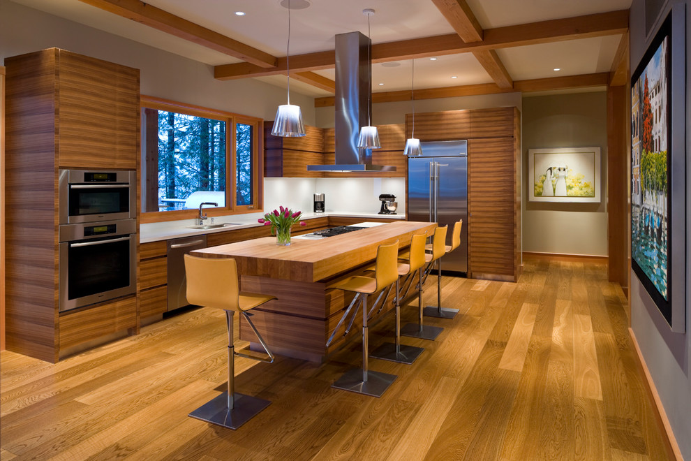 Foto på ett mellanstort funkis kök, med en undermonterad diskho, släta luckor, skåp i mellenmörkt trä, vitt stänkskydd, rostfria vitvaror, mellanmörkt trägolv, en köksö, träbänkskiva och glaspanel som stänkskydd