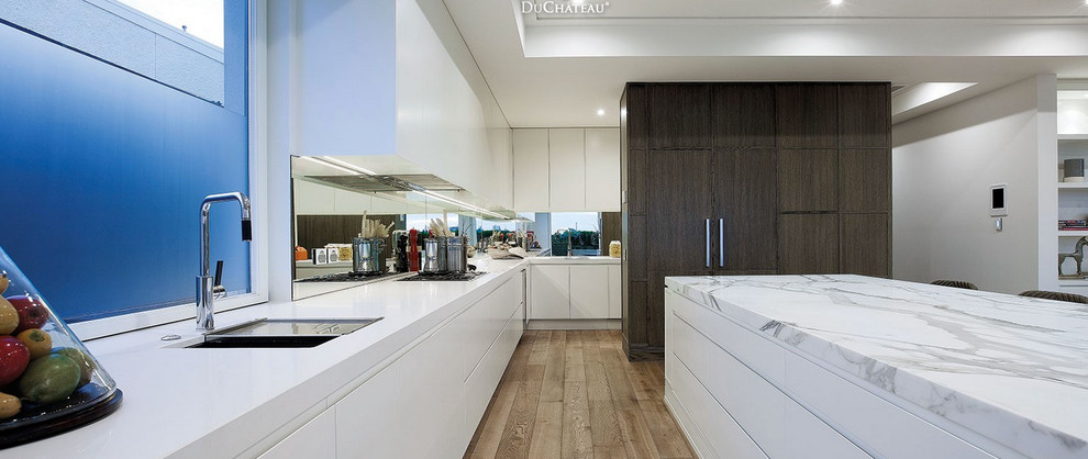 This is an example of a medium sized contemporary galley kitchen/diner in Houston with a single-bowl sink, flat-panel cabinets, white cabinets, marble worktops, metallic splashback, mirror splashback, integrated appliances, light hardwood flooring and an island.