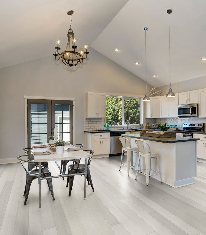 Example of a mid-sized transitional l-shaped gray floor eat-in kitchen design in Vancouver with an undermount sink, shaker cabinets, white cabinets, white backsplash, subway tile backsplash, stainless steel appliances, an island and black countertops