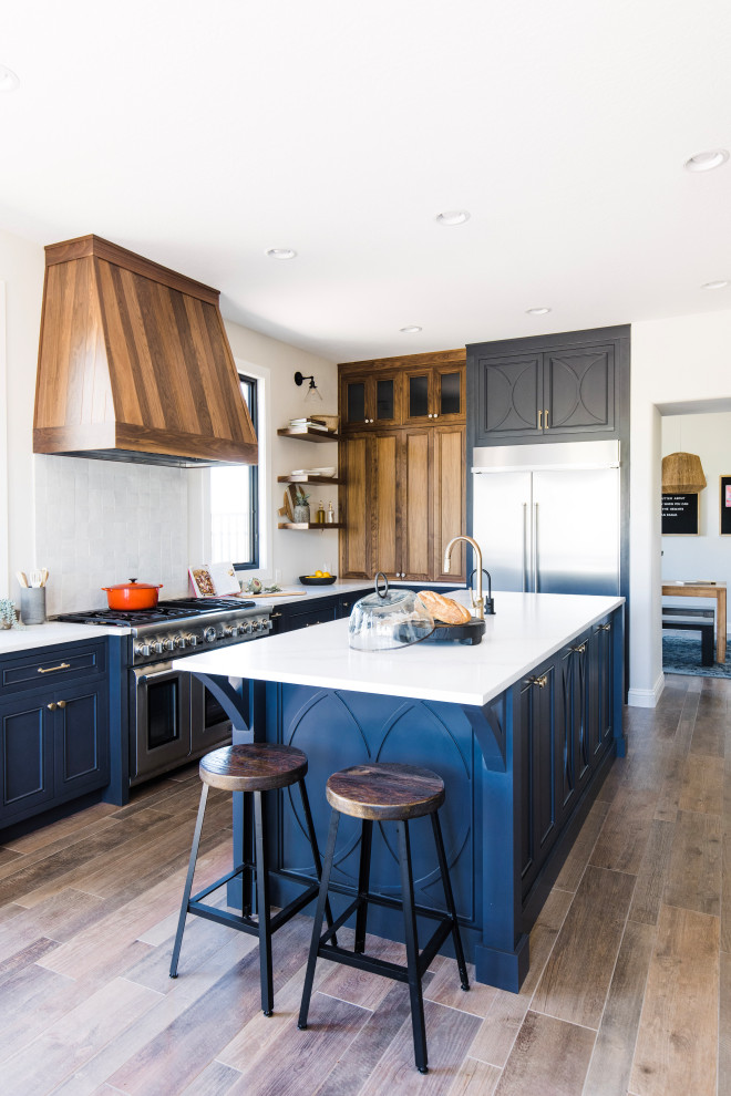 Inspiration for a classic l-shaped kitchen in Phoenix with recessed-panel cabinets, blue cabinets, stainless steel appliances, dark hardwood flooring, an island, brown floors and white worktops.
