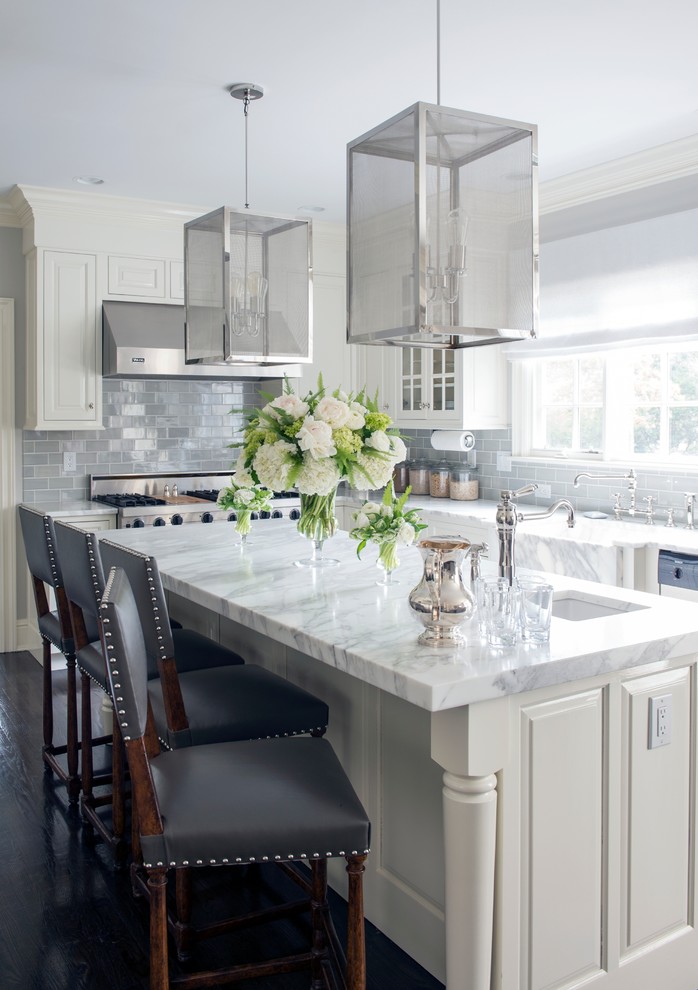 Klassisk inredning av ett mellanstort kök, med en undermonterad diskho, luckor med upphöjd panel, vita skåp, marmorbänkskiva, grått stänkskydd, stänkskydd i glaskakel, rostfria vitvaror, mörkt trägolv, en köksö och brunt golv
