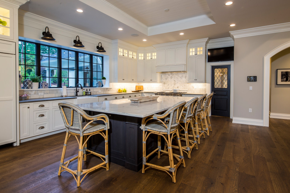 Example of a large transitional l-shaped medium tone wood floor and brown floor open concept kitchen design in Dallas with shaker cabinets, white cabinets, quartz countertops, white backsplash, marble backsplash, stainless steel appliances, an island, multicolored countertops and a farmhouse sink
