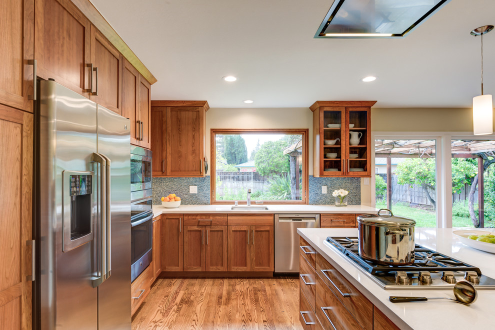 Bild på ett mellanstort vintage kök, med en undermonterad diskho, skåp i shakerstil, bänkskiva i kvarts, blått stänkskydd, rostfria vitvaror, en köksö, skåp i mellenmörkt trä, stänkskydd i mosaik, mellanmörkt trägolv och brunt golv