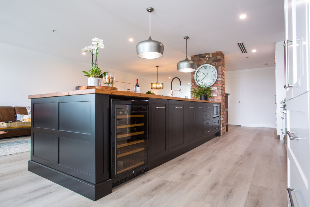Expansive rustic galley kitchen/diner in Brisbane with a double-bowl sink, recessed-panel cabinets, black cabinets, wood worktops, black splashback, metro tiled splashback, black appliances, an island, grey floors and white worktops.