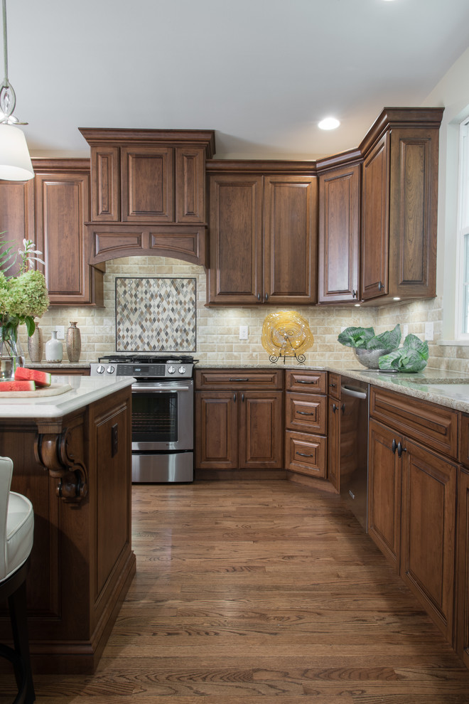 Large traditional l-shaped kitchen/diner in St Louis with a submerged sink, raised-panel cabinets, medium wood cabinets, engineered stone countertops, beige splashback, metro tiled splashback, stainless steel appliances, medium hardwood flooring and an island.