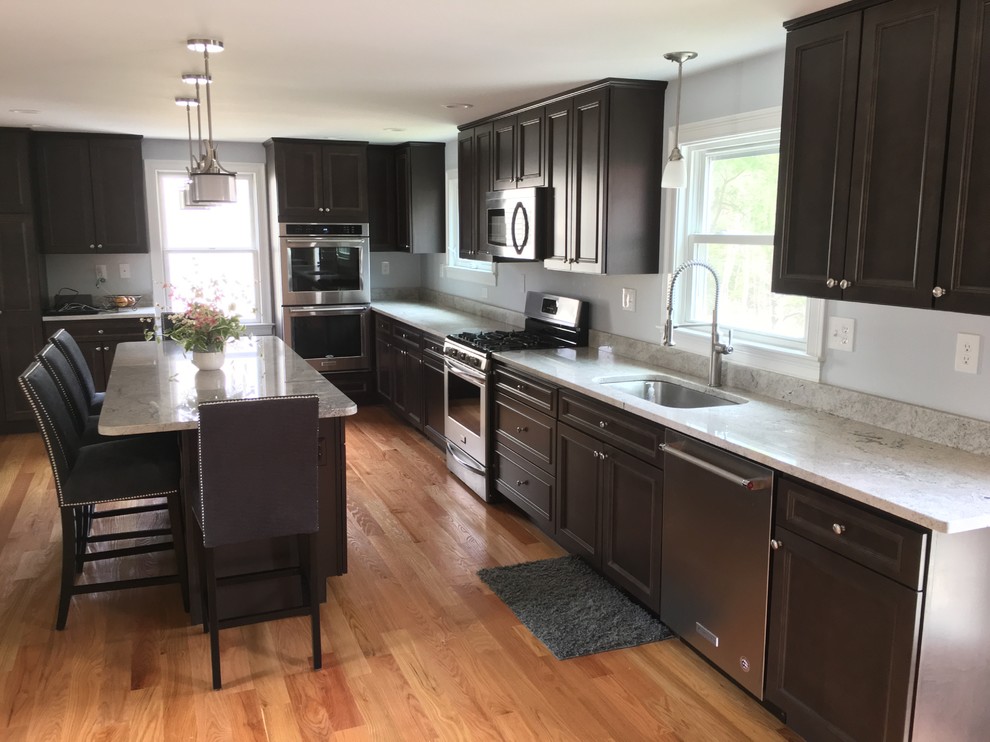 Example of a large classic u-shaped light wood floor and brown floor kitchen pantry design in Boston with an undermount sink, raised-panel cabinets, dark wood cabinets, granite countertops, gray backsplash, stone slab backsplash, stainless steel appliances and an island
