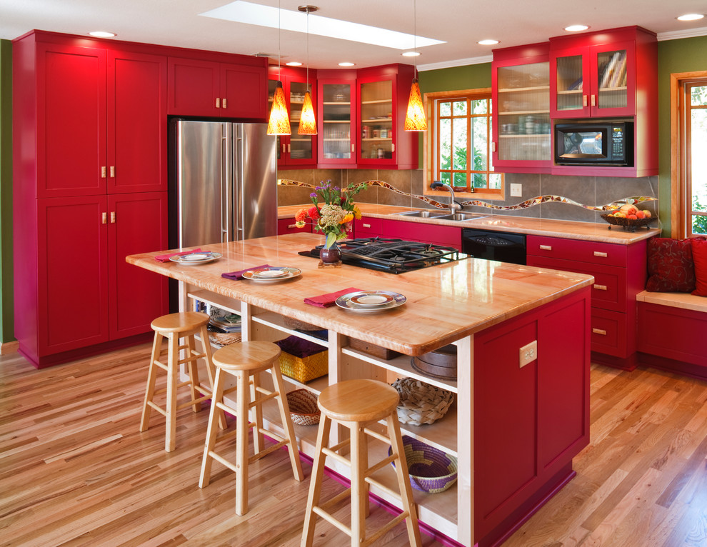 Klassische Küche in L-Form mit Doppelwaschbecken, Schrankfronten im Shaker-Stil, roten Schränken, Küchenrückwand in Grau, Küchengeräten aus Edelstahl, hellem Holzboden, Kücheninsel und Arbeitsplatte aus Holz in Sonstige
