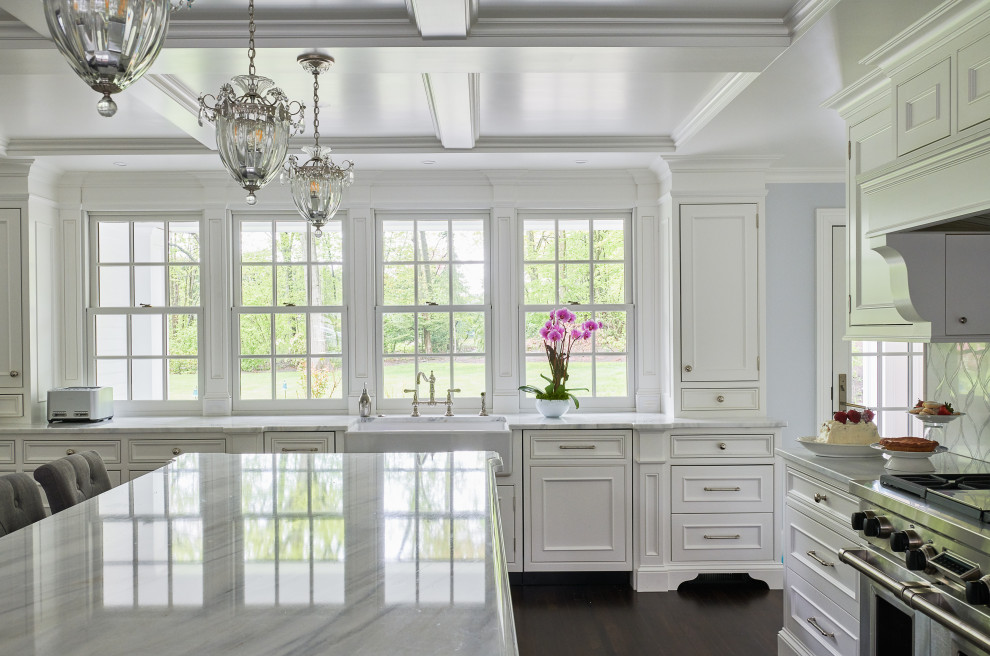 Klassisk inredning av ett vit vitt kök, med en rustik diskho, luckor med profilerade fronter, vita skåp, marmorbänkskiva, vitt stänkskydd, stänkskydd i mosaik, rostfria vitvaror, mellanmörkt trägolv och en köksö