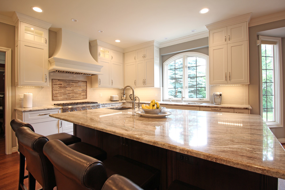 Example of a large transitional u-shaped medium tone wood floor and brown floor open concept kitchen design in Detroit with an undermount sink, shaker cabinets, white cabinets, granite countertops, gray backsplash, ceramic backsplash, stainless steel appliances, an island and multicolored countertops