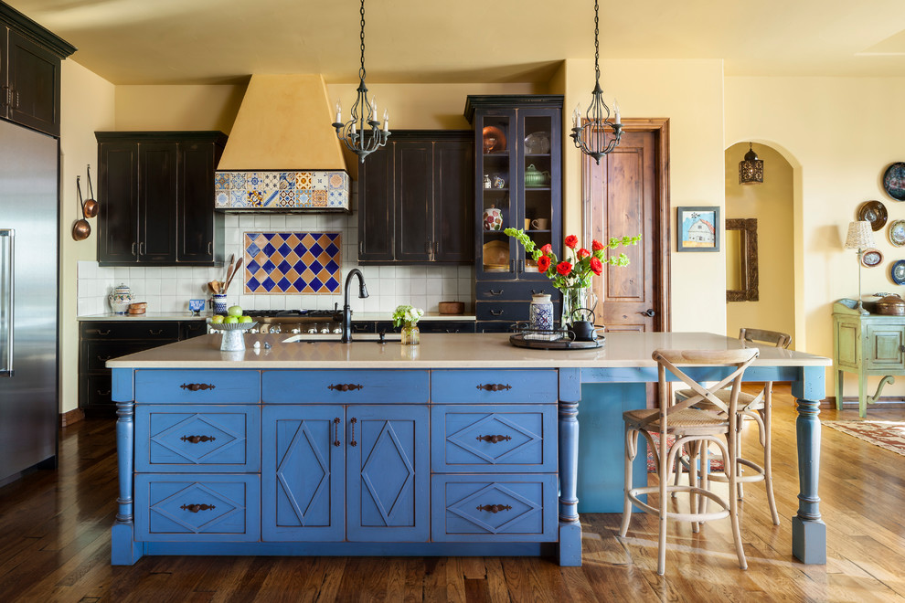 Exemple d'une cuisine sud-ouest américain en L avec un évier encastré, un placard à porte shaker, des portes de placard bleues, une crédence multicolore, un électroménager en acier inoxydable, un sol en bois brun, îlot, un sol marron et un plan de travail beige.