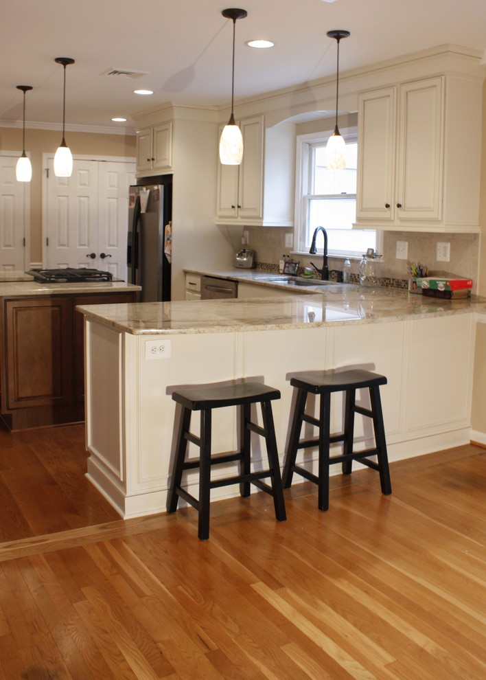 Mittelgroße Klassische Wohnküche in L-Form mit Doppelwaschbecken, profilierten Schrankfronten, weißen Schränken, Granit-Arbeitsplatte, Küchenrückwand in Beige, Küchengeräten aus Edelstahl, braunem Holzboden und Kücheninsel in Baltimore