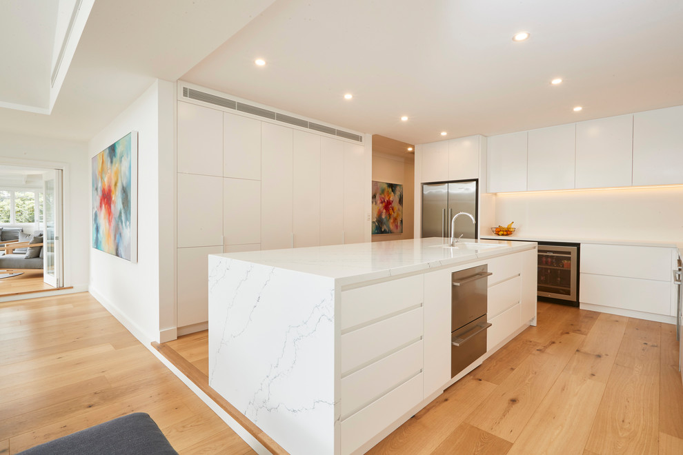 Inspiration for a medium sized modern galley kitchen/diner in Sydney with a submerged sink, flat-panel cabinets, white cabinets, marble worktops, white splashback, light hardwood flooring, an island and white worktops.