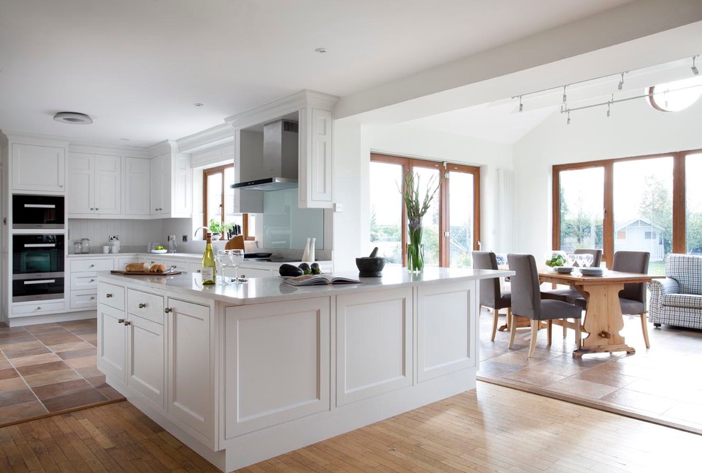 Exempel på ett klassiskt kök, med en undermonterad diskho, luckor med profilerade fronter, vita skåp, grått stänkskydd, stänkskydd i sten och rostfria vitvaror