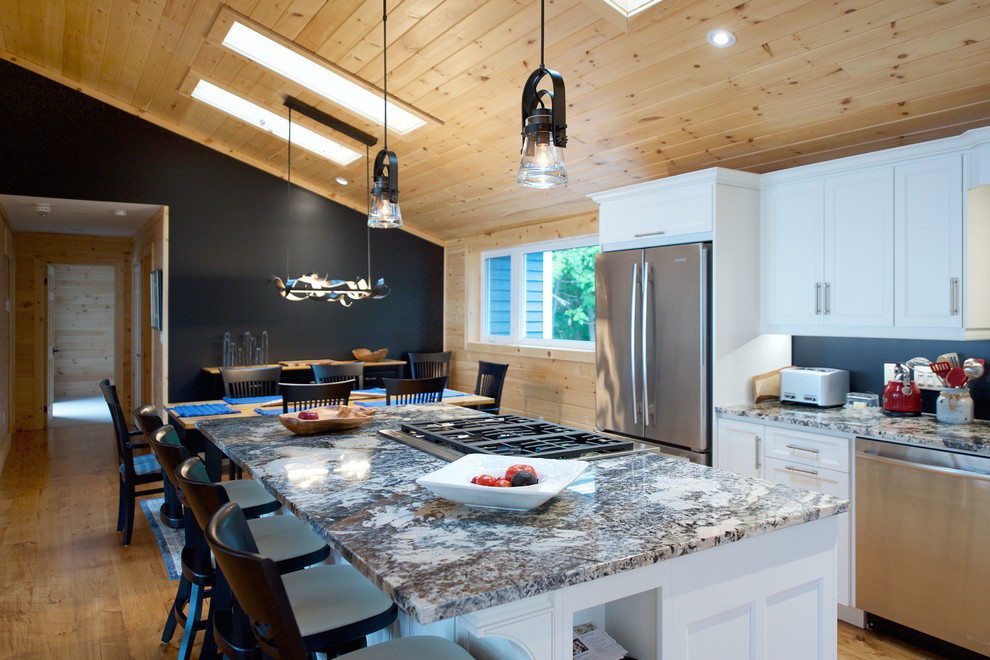 Exempel på ett mellanstort maritimt kök, med en undermonterad diskho, skåp i shakerstil, vita skåp, granitbänkskiva, svart stänkskydd, rostfria vitvaror, mellanmörkt trägolv och en köksö