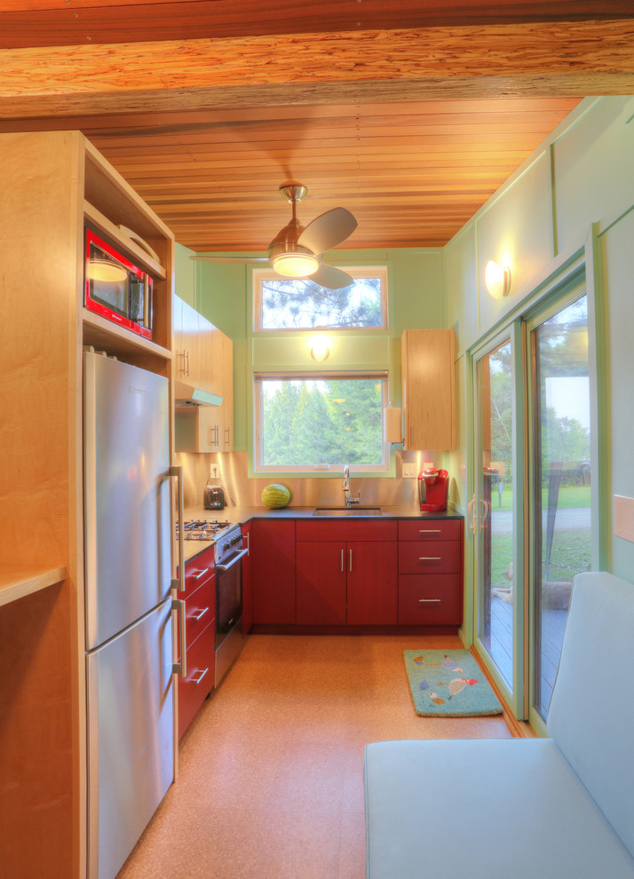 Foto på ett litet funkis kök, med en undermonterad diskho, släta luckor, röda skåp, bänkskiva i koppar, rostfria vitvaror och korkgolv