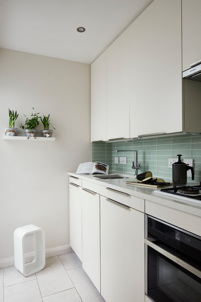 Bild på ett litet funkis vit linjärt vitt kök och matrum, med en enkel diskho, släta luckor, vita skåp, bänkskiva i kvartsit, grönt stänkskydd, stänkskydd i glaskakel, rostfria vitvaror, klinkergolv i keramik och vitt golv