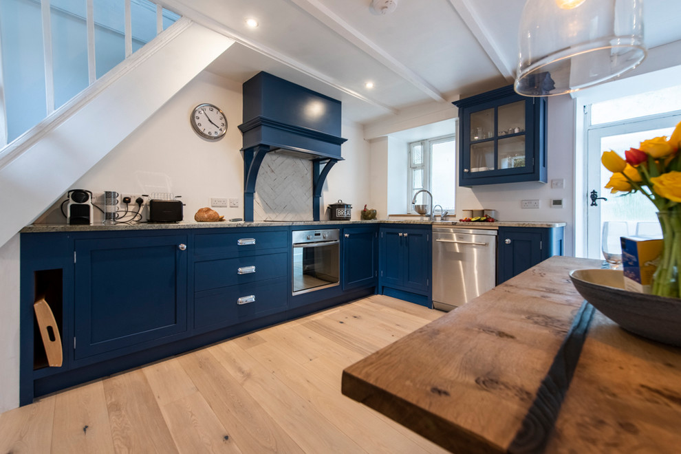 Immagine di una cucina moderna con ante con bugna sagomata, ante blu, top in granito, paraspruzzi bianco, elettrodomestici in acciaio inossidabile, pavimento in legno massello medio e top grigio