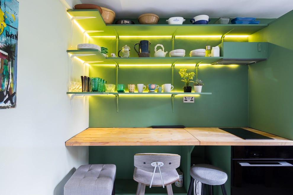 Bild på ett avskilt, litet beige linjärt beige kök, med en rustik diskho, öppna hyllor, gröna skåp, träbänkskiva, grönt stänkskydd, svarta vitvaror, klinkergolv i porslin och vitt golv