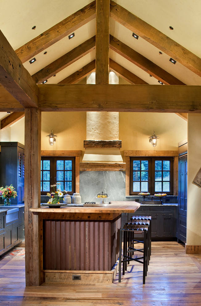 This is an example of a rustic u-shaped kitchen in Denver with an island, a belfast sink, shaker cabinets, distressed cabinets, soapstone worktops, stone slab splashback, integrated appliances and medium hardwood flooring.