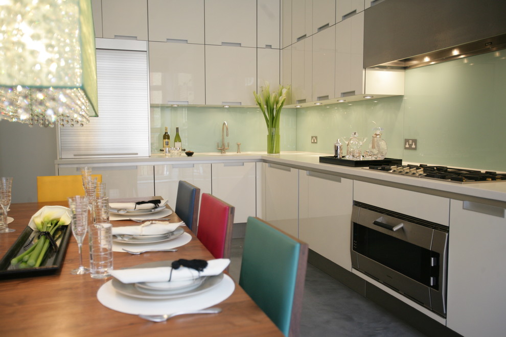 Inspiration for a large contemporary l-shaped kitchen/diner in London with an integrated sink, flat-panel cabinets, white cabinets, quartz worktops, green splashback, glass sheet splashback, stainless steel appliances, concrete flooring and no island.