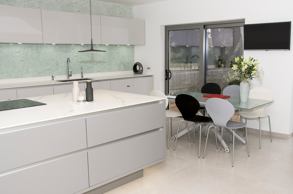 Immagine di una grande cucina minimalista con lavello integrato, ante lisce, ante grigie, top in superficie solida, paraspruzzi verde, paraspruzzi con lastra di vetro, elettrodomestici neri e pavimento in gres porcellanato