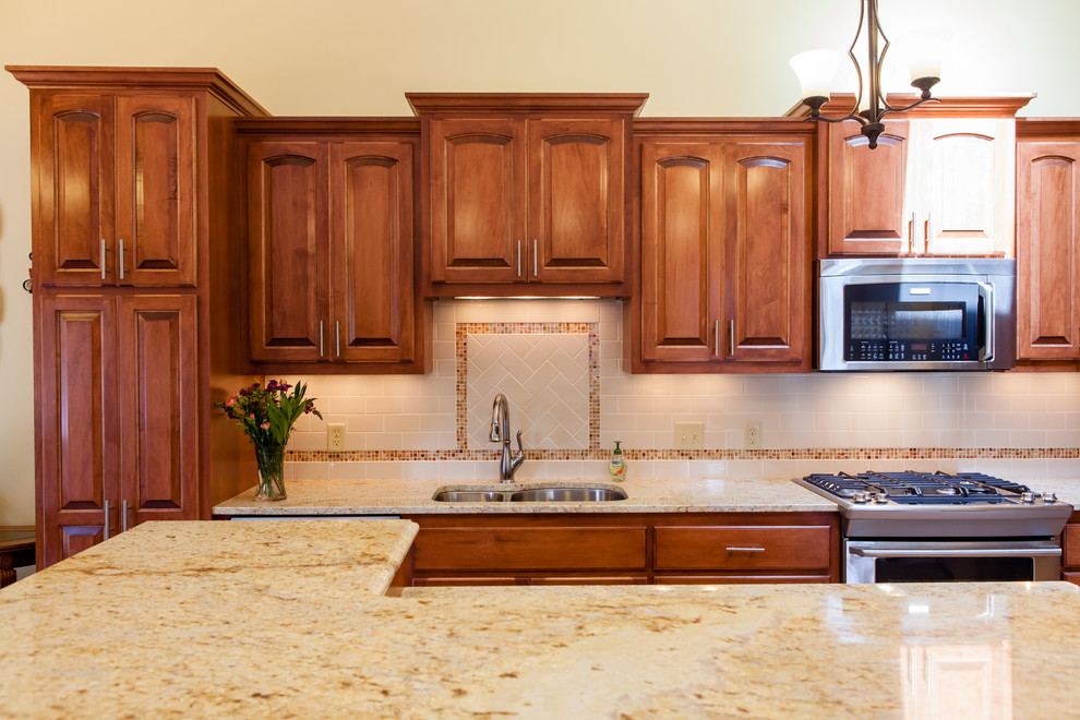 Exempel på ett mellanstort klassiskt kök, med en undermonterad diskho, luckor med upphöjd panel, skåp i mellenmörkt trä, granitbänkskiva, beige stänkskydd, stänkskydd i cementkakel, rostfria vitvaror, ljust trägolv och en köksö