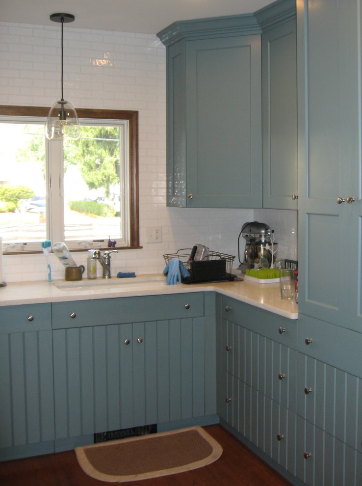 Foto på ett avskilt, litet amerikanskt vit u-kök, med en undermonterad diskho, skåp i shakerstil, blå skåp, bänkskiva i kvarts, vitt stänkskydd, stänkskydd i cementkakel, rostfria vitvaror, mellanmörkt trägolv och brunt golv