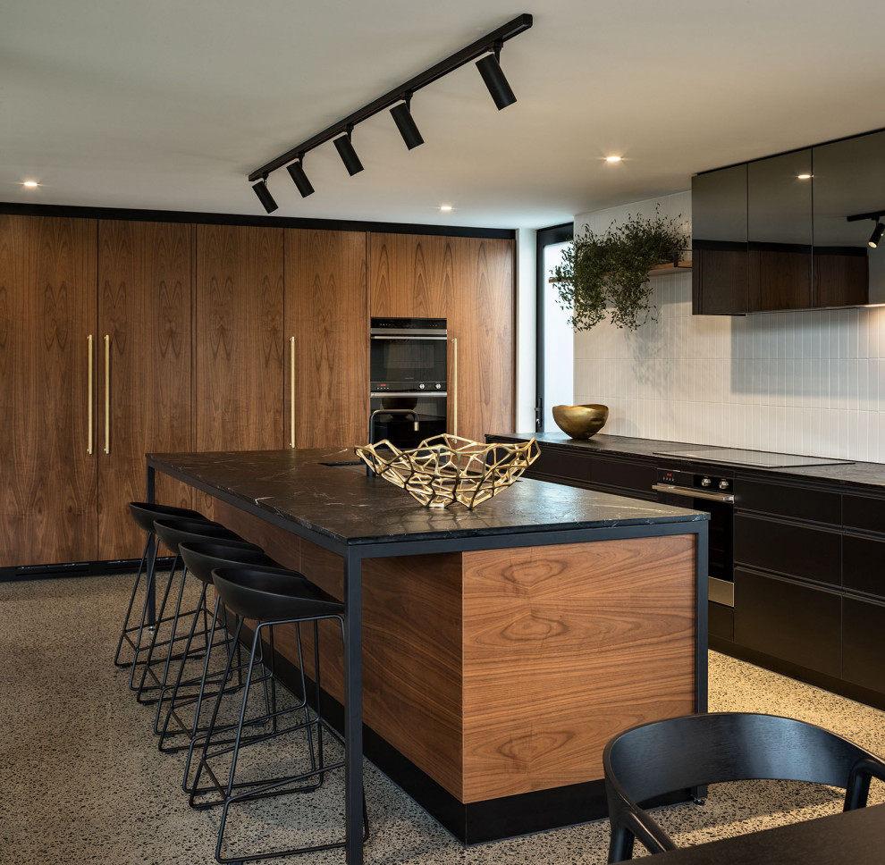 Eat-in kitchen - large contemporary l-shaped concrete floor and gray floor eat-in kitchen idea in Auckland with medium tone wood cabinets, granite countertops, white backsplash, ceramic backsplash, an island, black countertops, flat-panel cabinets and black appliances