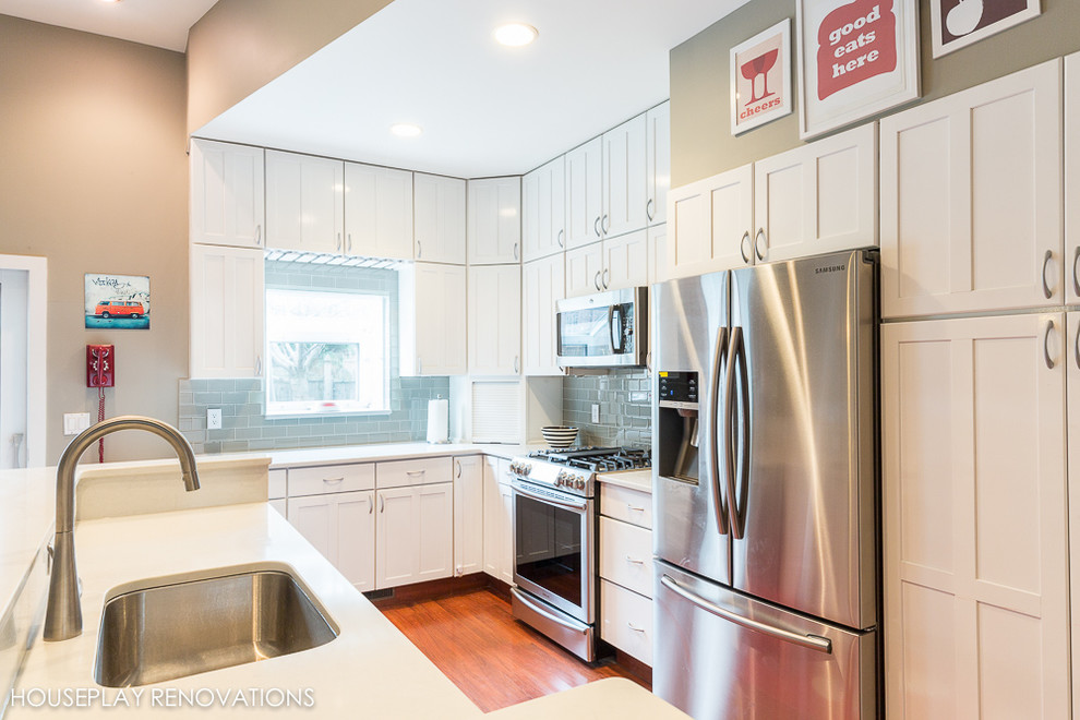 Exempel på ett mellanstort modernt linjärt kök och matrum, med en undermonterad diskho, bänkskiva i kvarts, stänkskydd i glaskakel, rostfria vitvaror, en köksö, skåp i shakerstil, vita skåp, blått stänkskydd och mellanmörkt trägolv