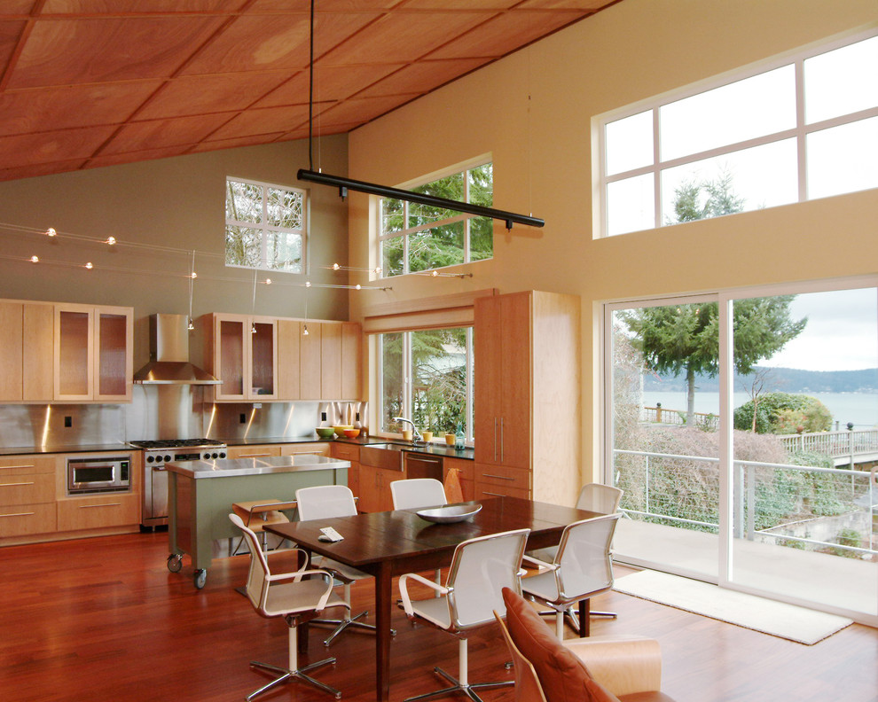 Modern inredning av ett kök, med en rustik diskho, släta luckor, skåp i ljust trä, stänkskydd med metallisk yta, rostfria vitvaror, stänkskydd i metallkakel, mellanmörkt trägolv och en köksö