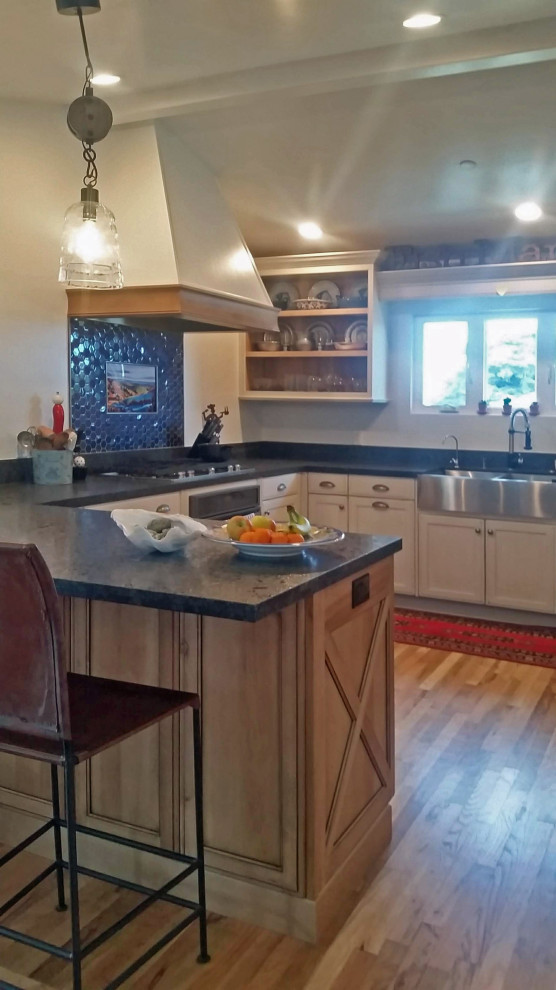 Mid-sized beach style u-shaped medium tone wood floor, beige floor and exposed beam eat-in kitchen photo in San Luis Obispo with a farmhouse sink, shaker cabinets, distressed cabinets, granite countertops, blue backsplash, ceramic backsplash, stainless steel appliances and black countertops